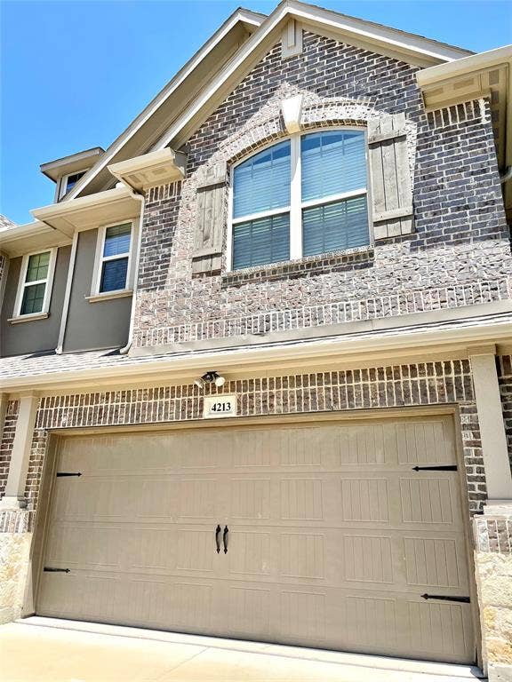 4213 Arbrook Way, Plano, TX 75074 Multi-story exterior featuring multi-toned brick masonry, arched window detailing with decorative wood-finish shutters, and a two-car panel garage door with decorative iron-style hardware