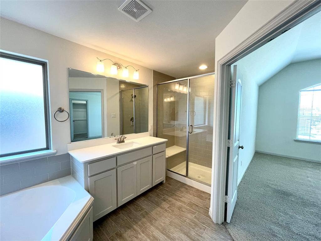 4213 Arbrook Way, Plano, TX 75074 Bathroom featuring a vanity with white countertop, shower enclosure with tiled surround and built-in bench, deep soaking tub, and wood-finish flooring