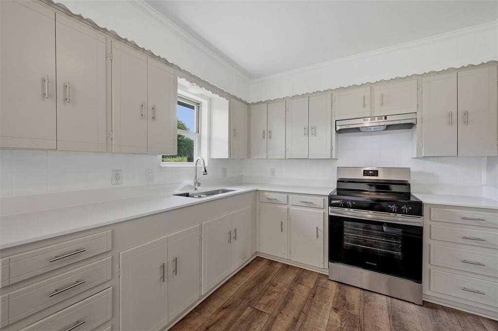 607 N Louisiana Drive, Celina, TX 75009 Kitchen featuring neutral-toned cabinetry, white countertops, stainless steel range with overhead vent hood, under-mount sink, and wood-finish flooring