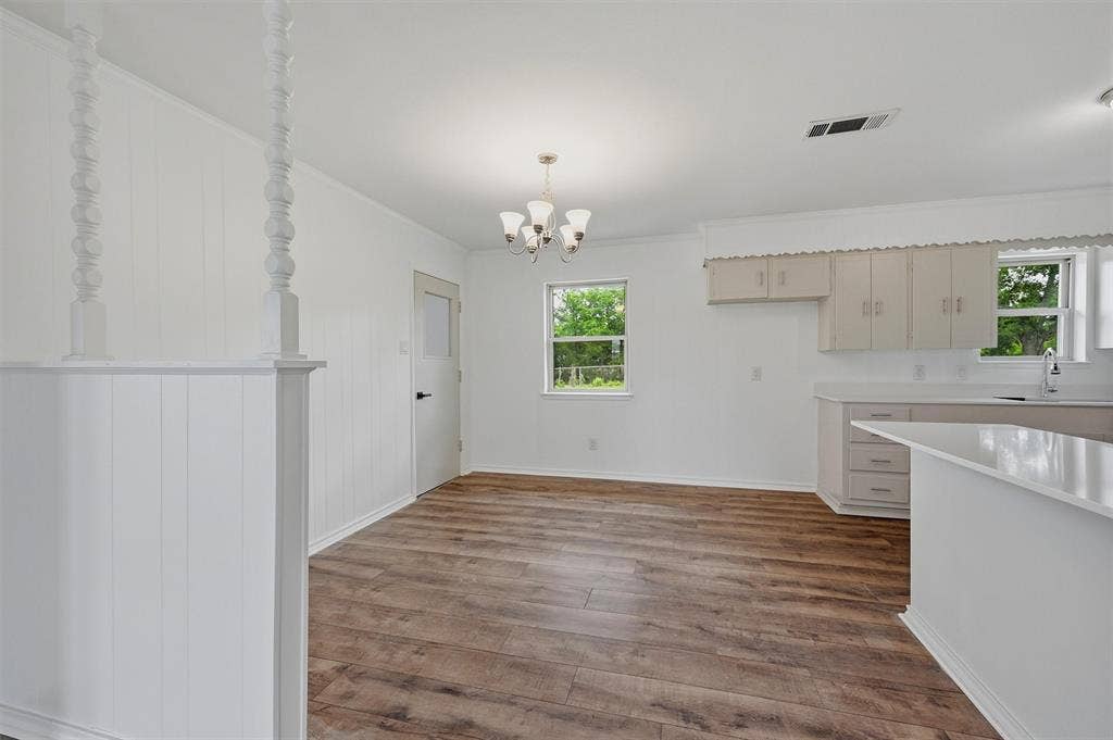 607 N Louisiana Drive, Celina, TX 75009 Interior space featuring wood-finish flooring, a multi-arm chandelier, decorative spindle room divider, and cabinetry with stone countertops