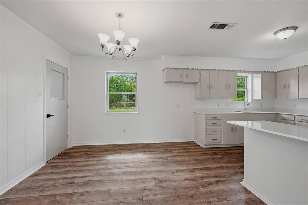 607 N Louisiana Drive, Celina, TX 75009 Kitchen featuring light-toned cabinetry, solid surface countertops, wood-finish flooring, a multi-arm chandelier, and a neutral color palette