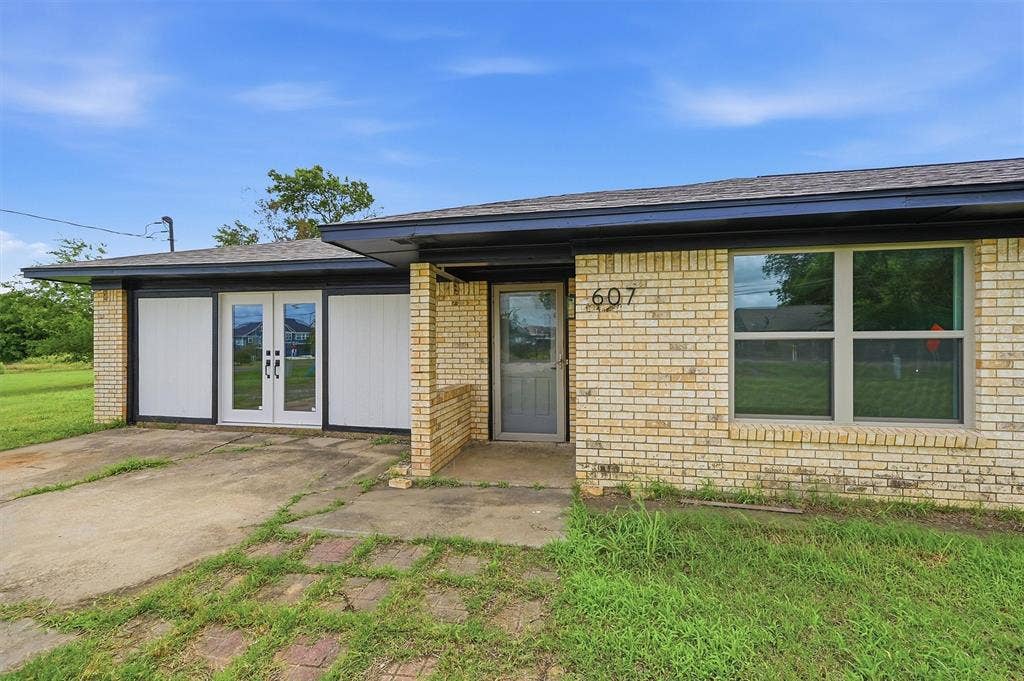 607 N Louisiana Drive, Celina, TX 75009 Single-story exterior featuring light-toned brick masonry, a low-pitch roofline, double glass-pane entry doors, and large windows