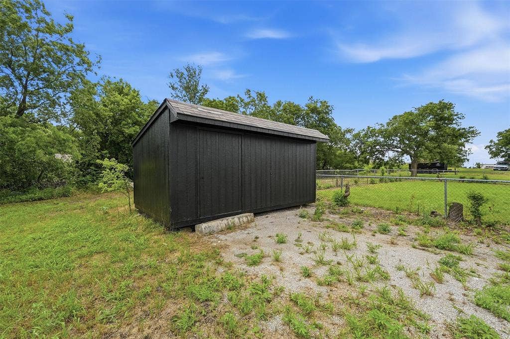 607 N Louisiana Drive, Celina, TX 75009 Black painted exterior storage structure featuring a pitched roof, vertical siding, and a gravel pad foundation