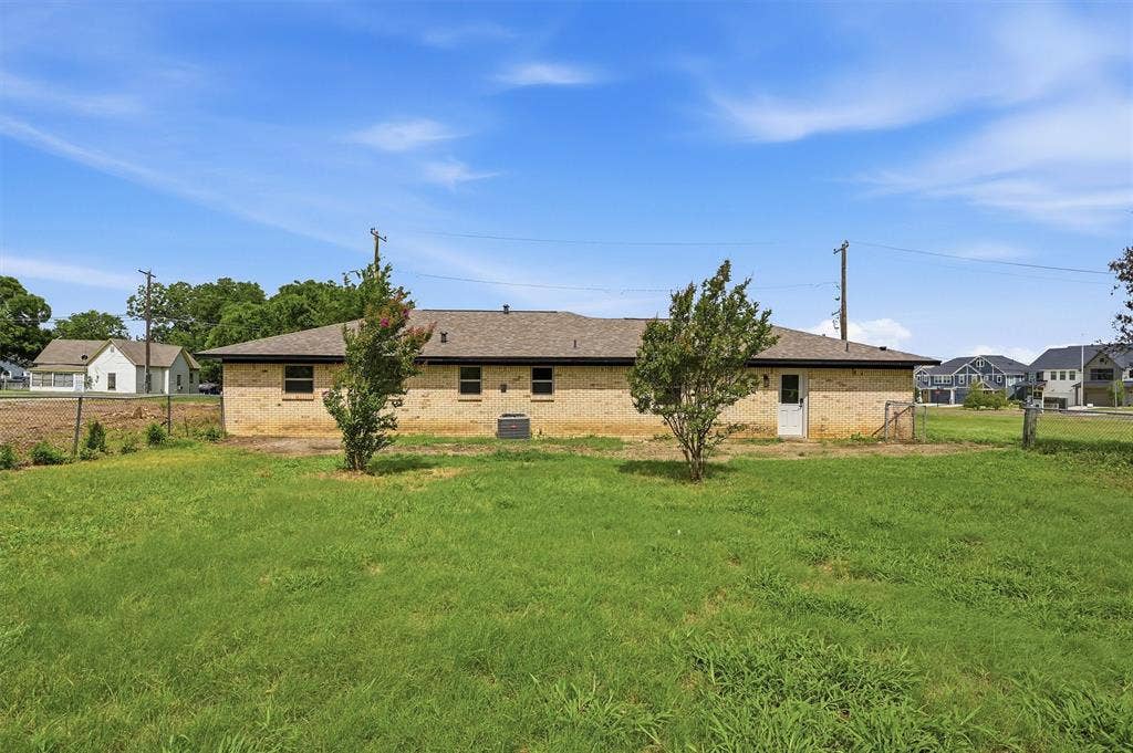 607 N Louisiana Drive, Celina, TX 75009 Single-story residence featuring a brick exterior, hipped roof, grass-covered backyard, and mature trees