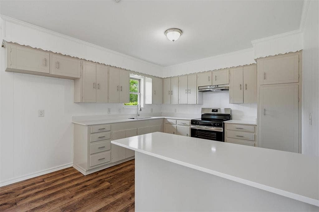 607 N Louisiana Drive, Celina, TX 75009 Kitchen featuring light-toned cabinetry, solid-surface countertops, wood-finish flooring, a stainless steel range, and a breakfast bar