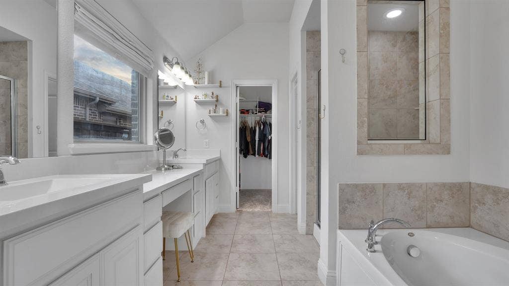 124 Village Creek Drive, McKinney, TX 75071 Double vanity with white cabinetry, quartz-surface countertops, soaking tub with tile surround, and neutral-tone tile flooring