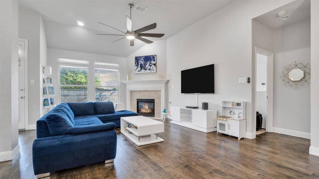 124 Village Creek Drive, McKinney, TX 75071 Living room featuring vaulted ceilings, wood-finish flooring, a fireplace with a decorative mantel, and a multi-blade ceiling fan