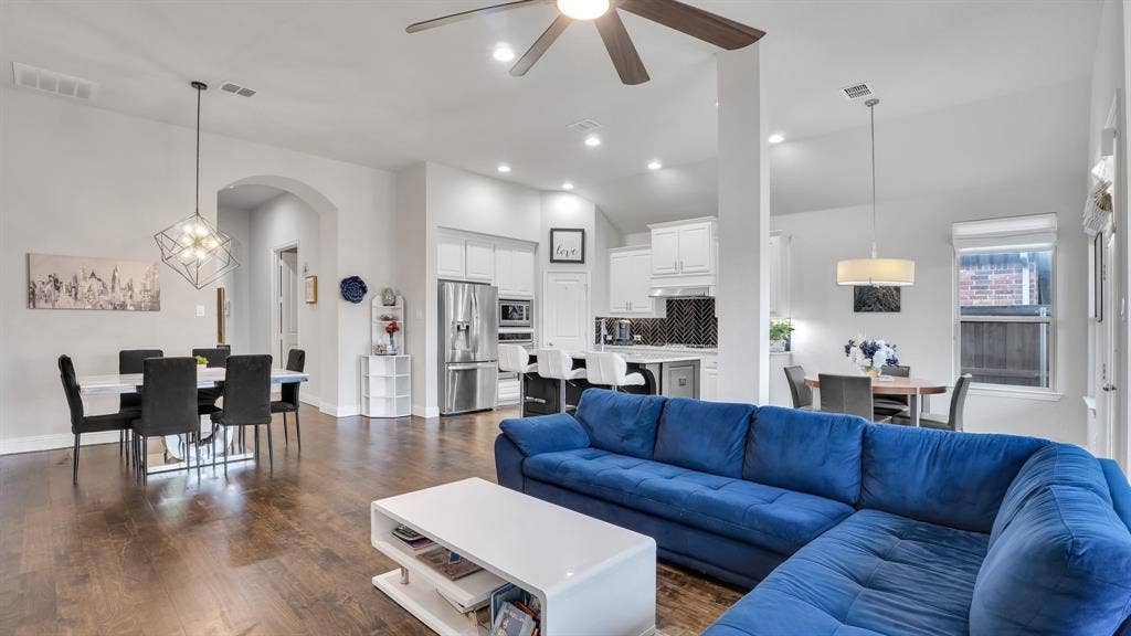 124 Village Creek Drive, McKinney, TX 75071 Open-concept interior featuring wood-finish flooring, vaulted ceilings, white cabinetry, a kitchen island with seating, and geometric pendant lighting