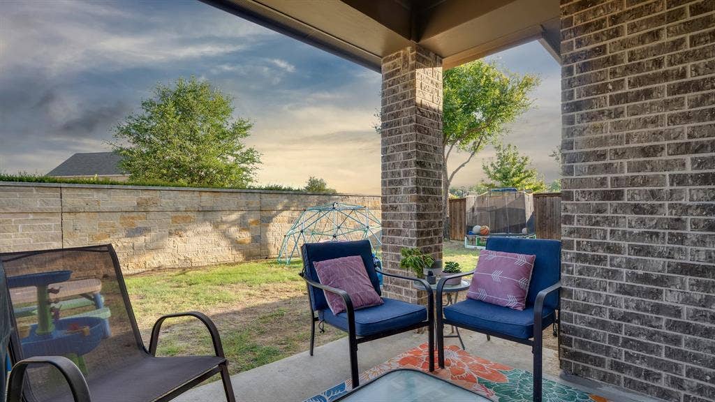 124 Village Creek Drive, McKinney, TX 75071 Covered patio featuring a concrete floor and brick structural pillar, opening to a private backyard enclosed by a stone perimeter wall