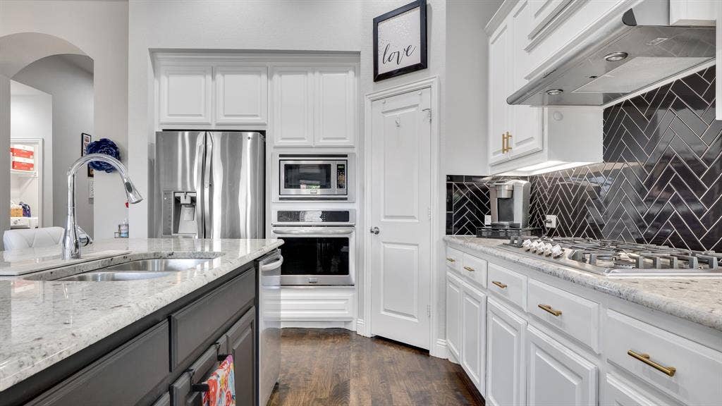 124 Village Creek Drive, McKinney, TX 75071 Kitchen featuring white shaker-style cabinetry, stone countertops, stainless steel appliances, built-in wall oven and microwave, and black herringbone-patterned tile backsplash