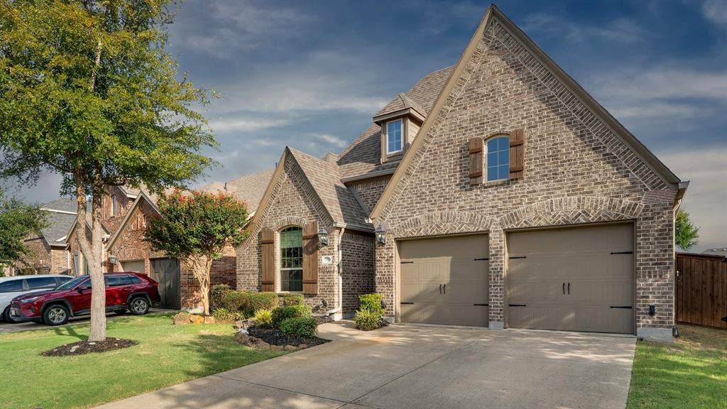 124 Village Creek Drive, McKinney, TX 75071 Brick exterior with multiple gables, arch-top windows, decorative wood shutters, and an attached two-car garage