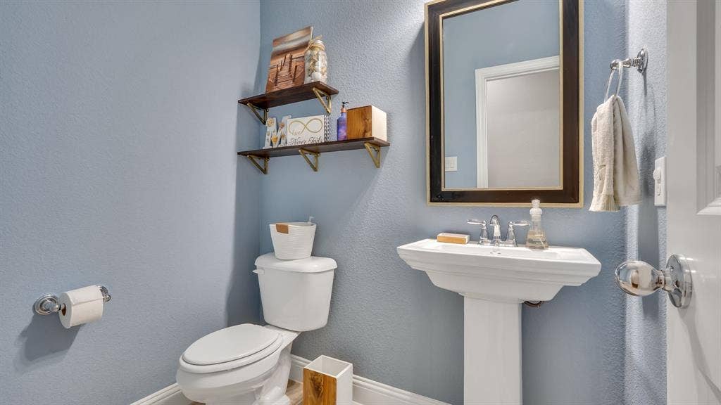 124 Village Creek Drive, McKinney, TX 75071 Pedestal sink with polished chrome widespread faucet, framed wall mirror, and two wall-mounted wooden shelves with metal brackets