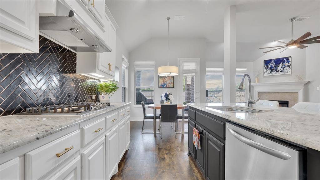 124 Village Creek Drive, McKinney, TX 75071 Kitchen featuring white shaker-style cabinetry, black herringbone tile backsplash, stone-finish countertops, stainless steel appliances, and wood-finish flooring