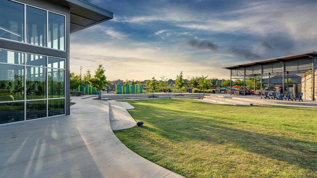 124 Village Creek Drive, McKinney, TX 75071 Contemporary multi-purpose common area featuring a floor-to-ceiling glass-walled structure, expansive manicured lawn, tiered concrete amphitheater, and a covered pavilion with metal roof framing
