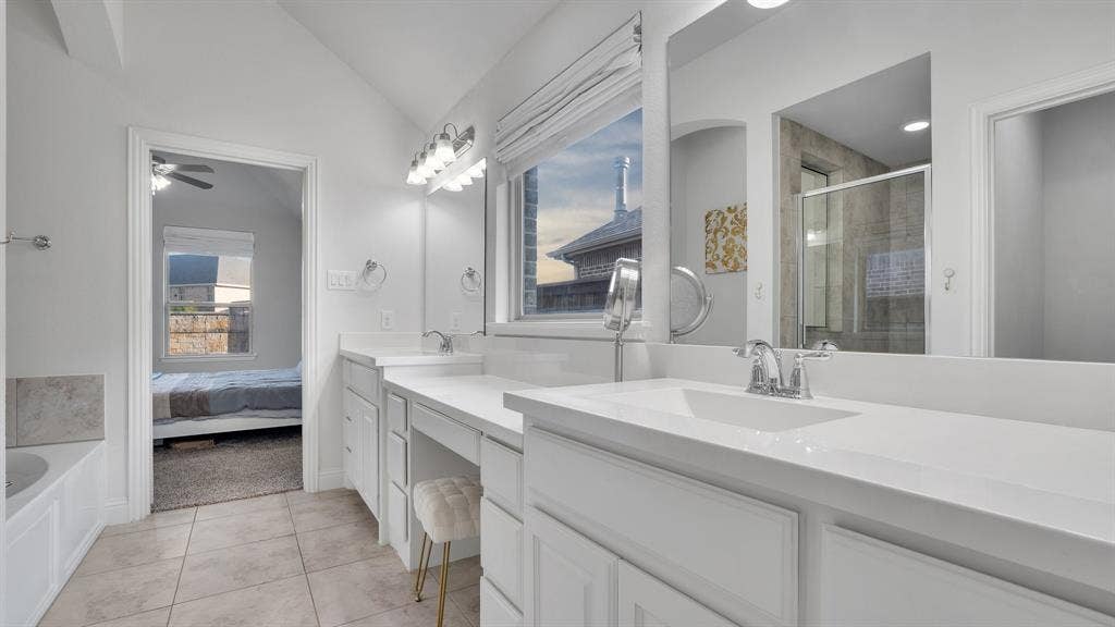 124 Village Creek Drive, McKinney, TX 75071 Bathroom featuring a dual-sink vanity with white cabinetry and solid-surface countertops, large wall-mounted mirrors, tile flooring, and a soaking tub
