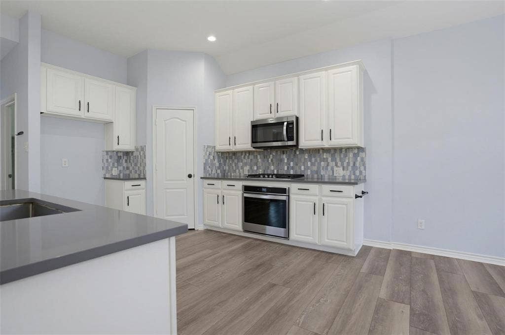 1402 Bradford Trace Drive, Allen, TX 75002 Kitchen featuring white cabinetry, solid surface countertops, a mosaic tile backsplash, stainless steel appliances, and wood-finish flooring