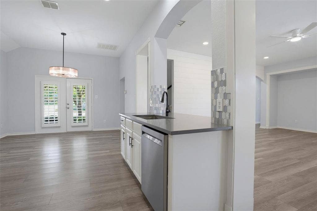 1402 Bradford Trace Drive, Allen, TX 75002 Kitchen featuring a peninsula with solid-surface countertops, stainless steel dishwasher, and a faucet with a pull-down sprayer, accented by a hexagonal tile backsplash and wood-finish flooring throughout