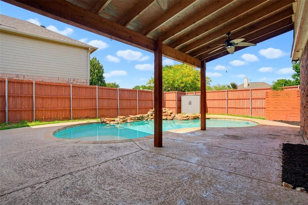 1402 Bradford Trace Drive, Allen, TX 75002 Covered concrete patio with a wooden beam ceiling and ceiling fan, featuring a swimming pool with a rock water feature enclosed by a wooden privacy fence