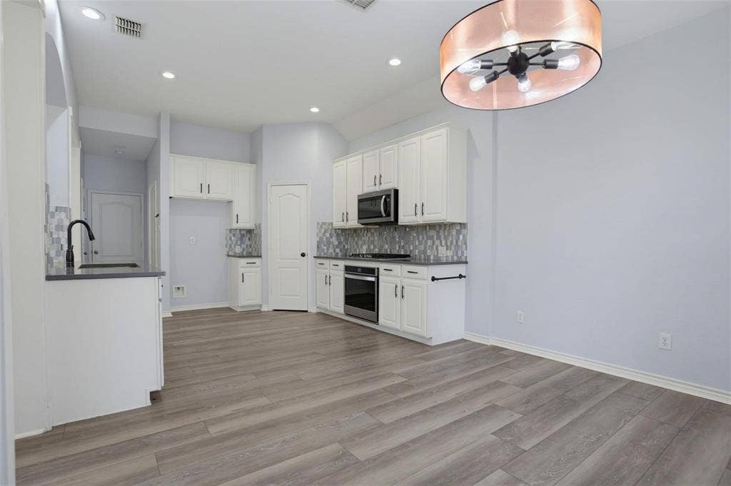 1402 Bradford Trace Drive, Allen, TX 75002 Kitchen featuring white cabinetry, wood-finish flooring, stone-style tile backsplash, built-in stainless steel appliances, and a modern drum-style pendant light fixture