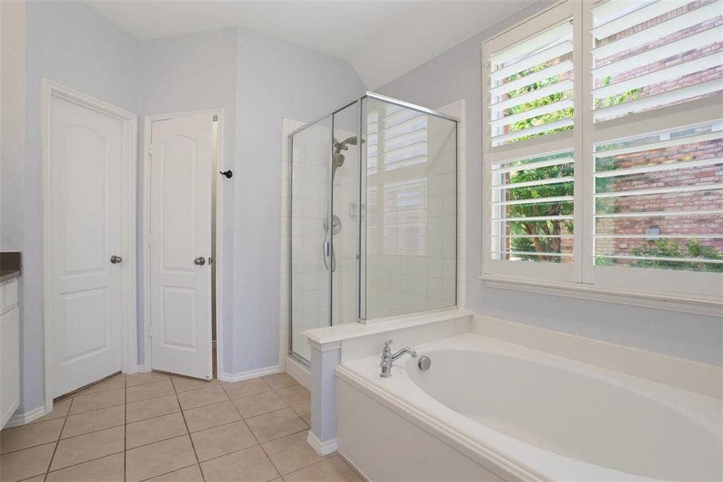 1402 Bradford Trace Drive, Allen, TX 75002 Bathroom featuring an oval soaking tub, separate glass-enclosed shower, tile flooring, and plantation shutters