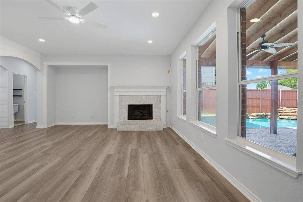 1402 Bradford Trace Drive, Allen, TX 75002 Living area featuring wood-finish flooring, a masonry fireplace with a white mantel, recessed lighting, and large windows with exterior pool and covered patio visibility