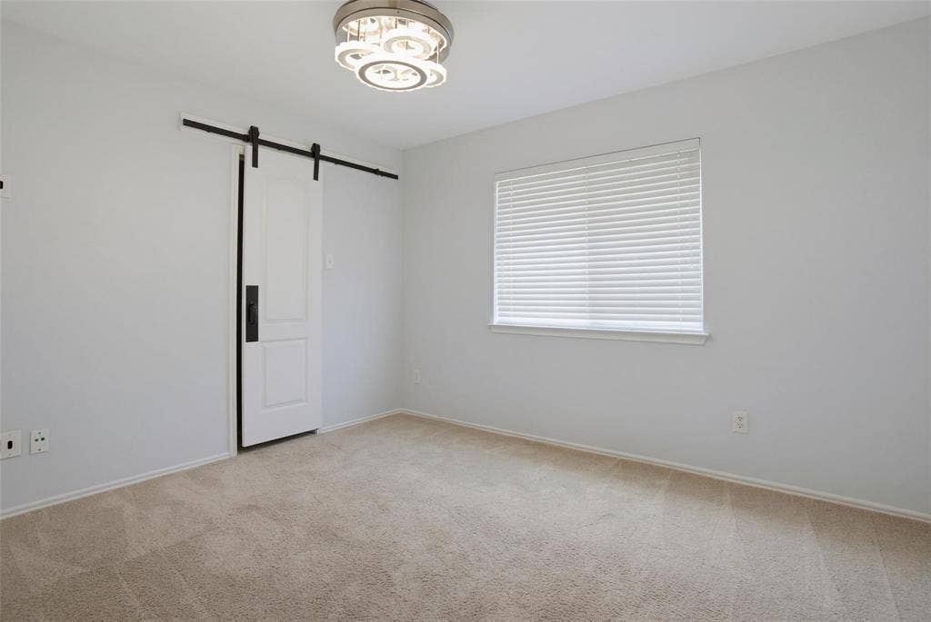 1402 Bradford Trace Drive, Allen, TX 75002 Room featuring neutral carpeting, a sliding barn-style door with matte black hardware, horizontal window blinds, and a modern circular tiered flush-mount light fixture