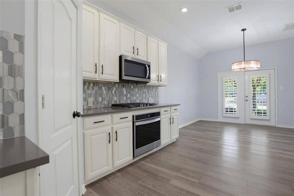 1402 Bradford Trace Drive, Allen, TX 75002 Kitchen featuring white cabinetry, solid-surface countertops, a mosaic tile backsplash, stainless steel appliances, and wood-finish flooring