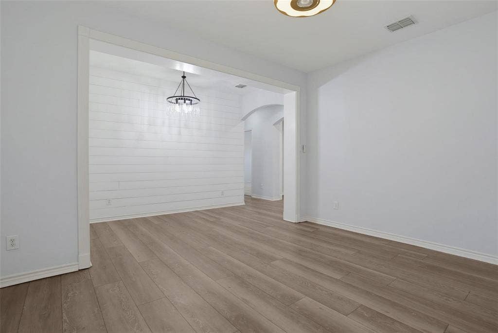 1402 Bradford Trace Drive, Allen, TX 75002 Interior space featuring wood-finish flooring, horizontal shiplap wall detailing, an overhead tiered chandelier, and arched architectural framing