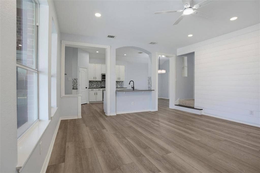 1402 Bradford Trace Drive, Allen, TX 75002 Open-concept interior featuring wood-finish flooring, shiplap wall detailing, arched architectural openings, recessed lighting, and a kitchen island with a matte black faucet