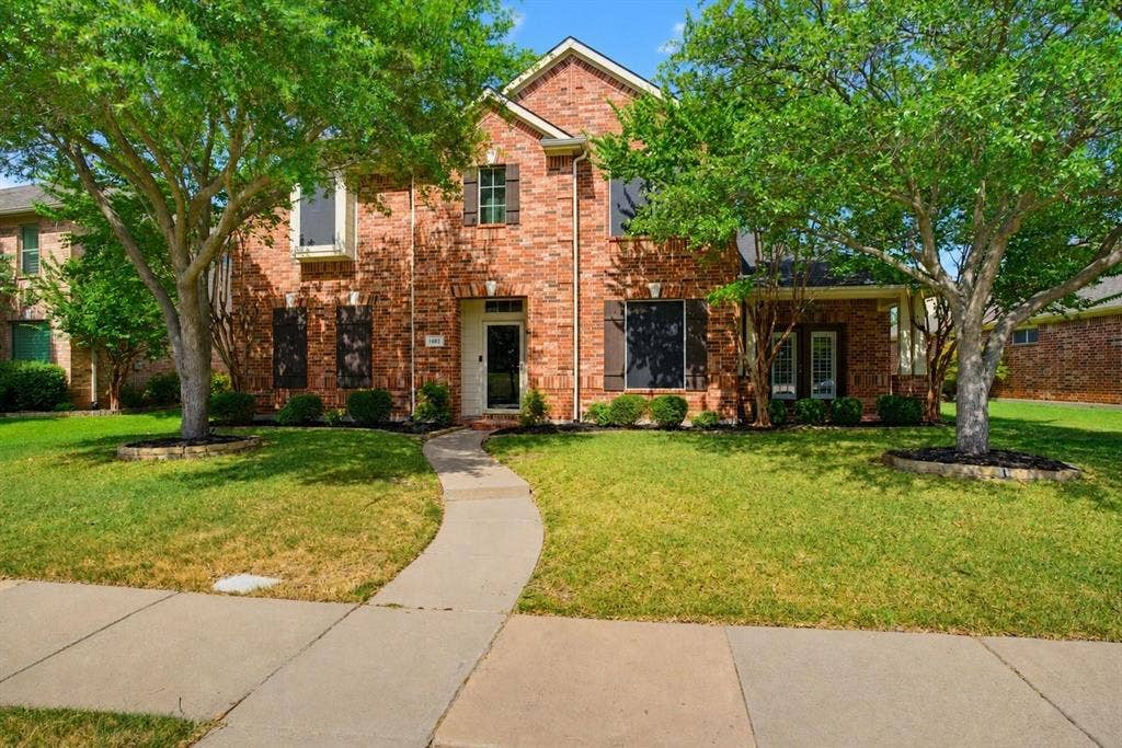 1402 Bradford Trace Drive, Allen, TX 75002 Two-story brick exterior featuring dark window shutters, a front entryway with a transom window, and a concrete walkway
