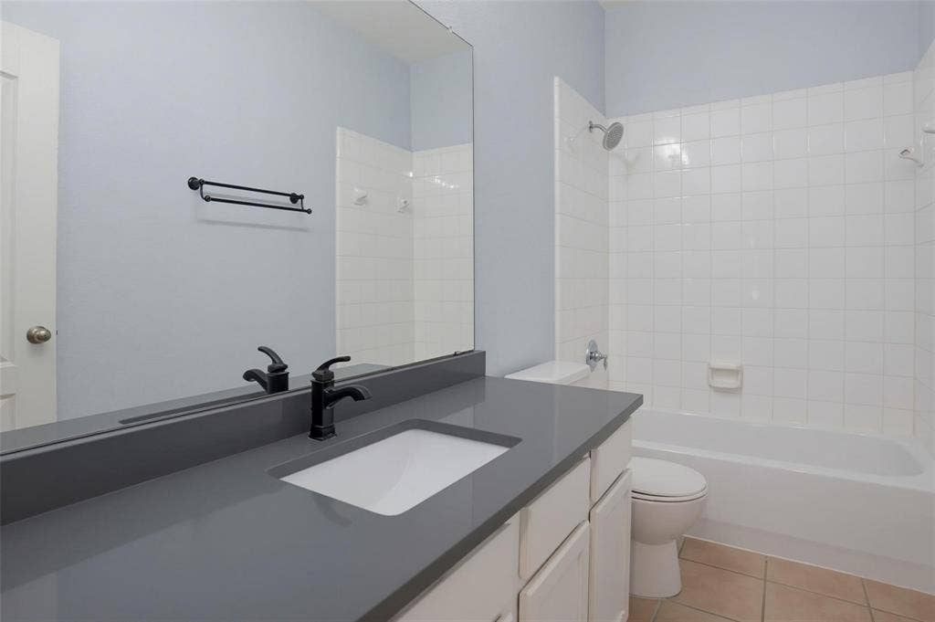 1402 Bradford Trace Drive, Allen, TX 75002 Bathroom featuring a vanity with a dark solid-surface countertop, an undermount sink, and matte black hardware, paired with a floor-to-ceiling mirror, a porcelain-tiled tub surround, and ceramic tile flooring