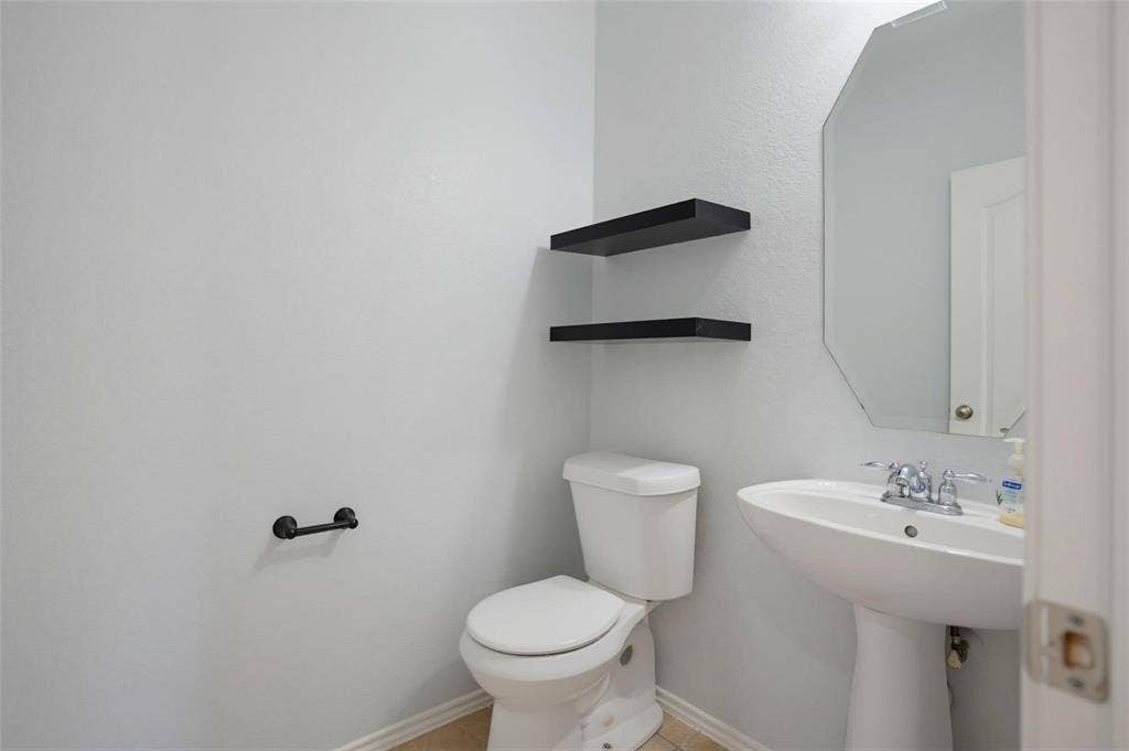1402 Bradford Trace Drive, Allen, TX 75002 Powder room featuring a pedestal sink, wall-mounted octagonal mirror, dual black floating shelves, and a matte black hardware finish