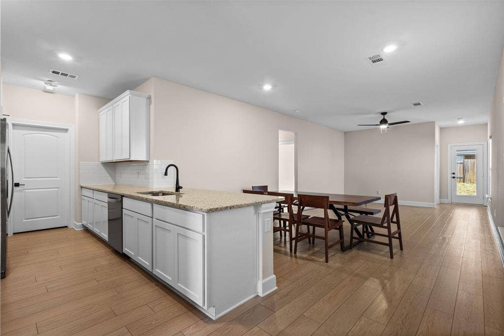 Kitchen featuring white shaker cabinetry, stone-finish countertops, stainless steel appliances, a high-arc matte black faucet, and wood-finish flooring throughout