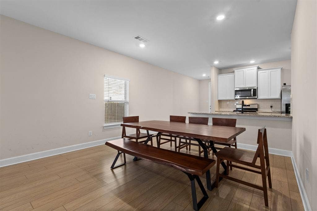 Open-concept area featuring wood-finish flooring, recessed lighting, and a kitchen equipped with white cabinetry, stone-finish countertops, and stainless steel appliances