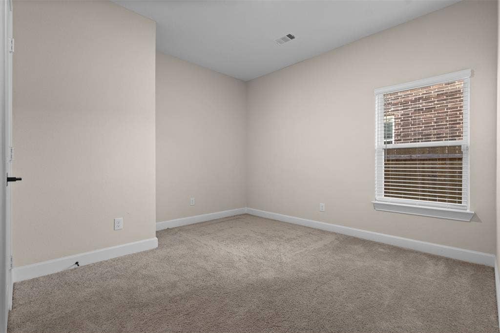 Neutral interior space featuring neutral wall paint, carpeted flooring, a single window with white horizontal blinds, and a solid interior door