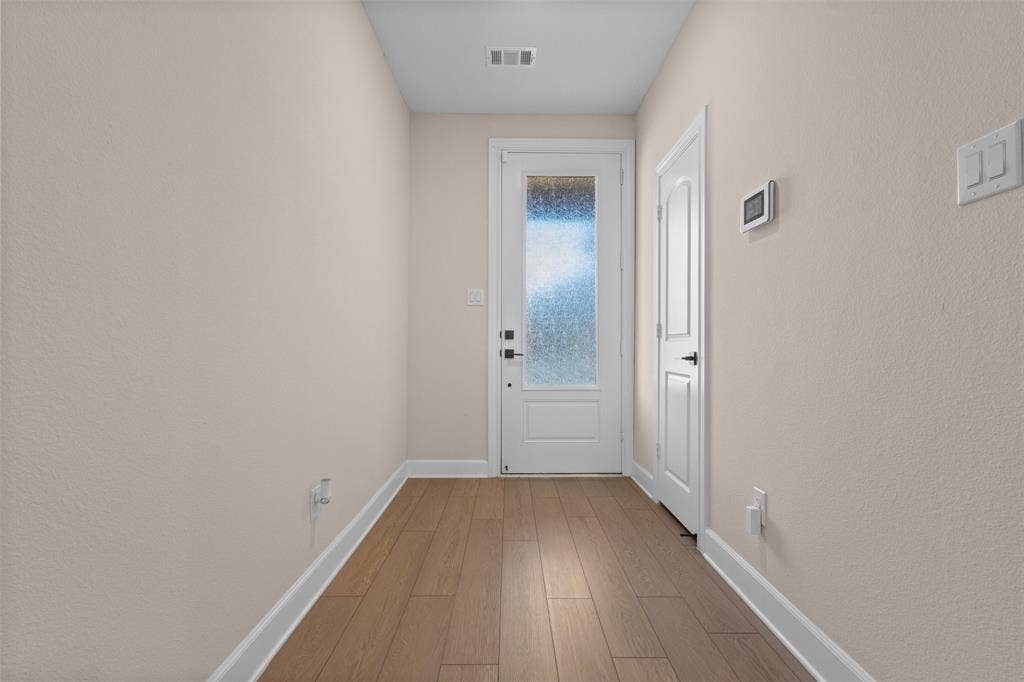 Entryway featuring wood-finish flooring, a white paneled door with a textured glass inlay, and matte black hardware