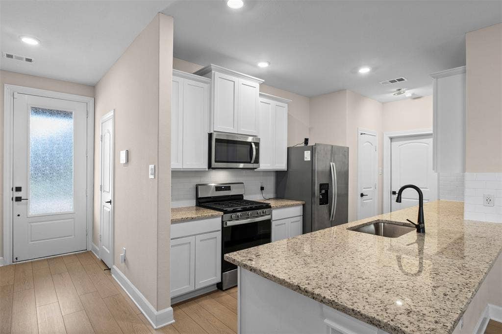 Kitchen featuring white cabinetry, stone-surface countertops, wood-finish flooring, stainless steel appliances, and a matte black faucet