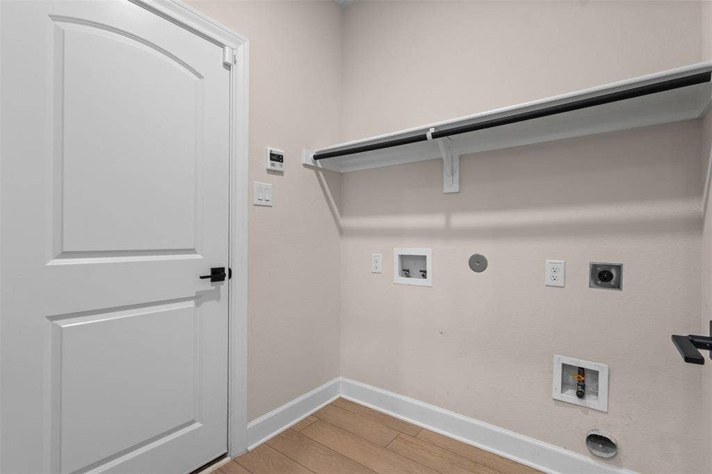 Utility room featuring wood-finish flooring, a white paneled door with matte black hardware, and an overhead built-in shelving unit with an integrated hanging rod