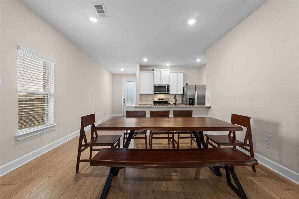 Open-concept kitchen featuring white shaker-style cabinetry, a stone-surfaced breakfast bar, stainless steel appliances, and wood-finish flooring