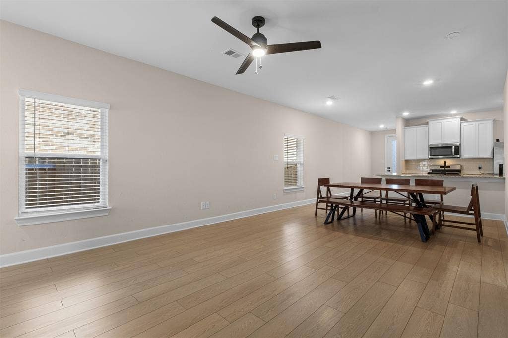 Open-concept interior featuring wood-finish flooring, recessed lighting, a modern ceiling fan, and white kitchen cabinetry with a breakfast bar