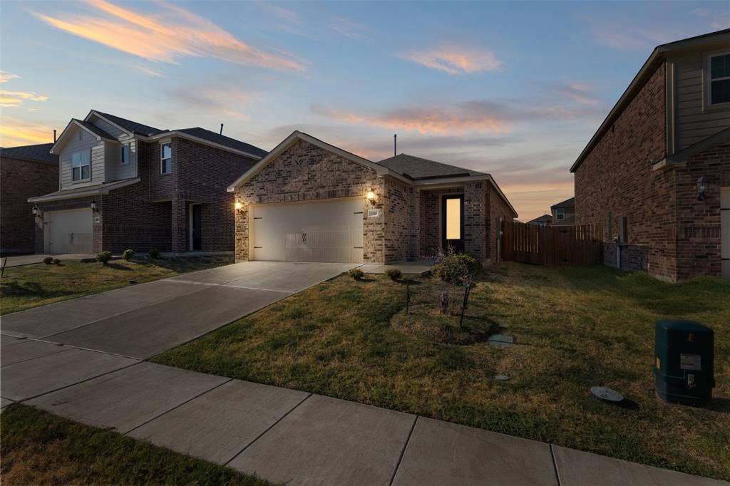 Single-story exterior featuring a brick facade, concrete driveway, attached two-car garage, and a covered entryway