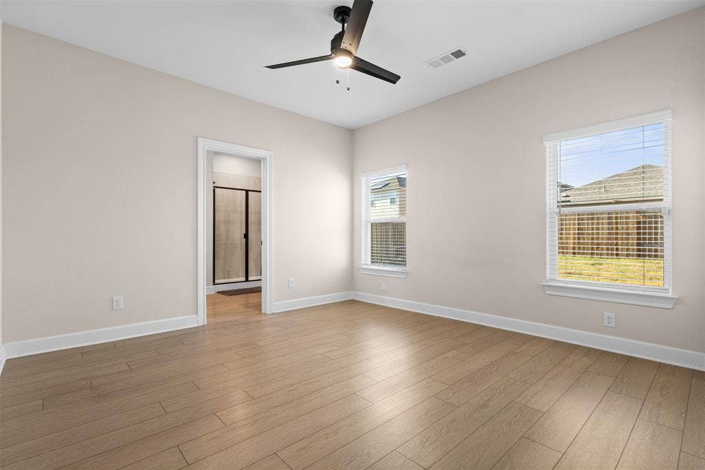 Neutral-toned interior featuring wood-finish flooring, a matte black ceiling fan with integrated lighting, and multiple windows with white horizontal blinds