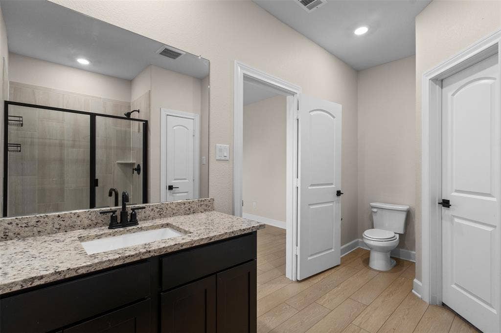 Bathroom featuring a dark wood-finish vanity with a stone countertop, an integrated rectangular sink, matte black hardware, and wood-finish flooring