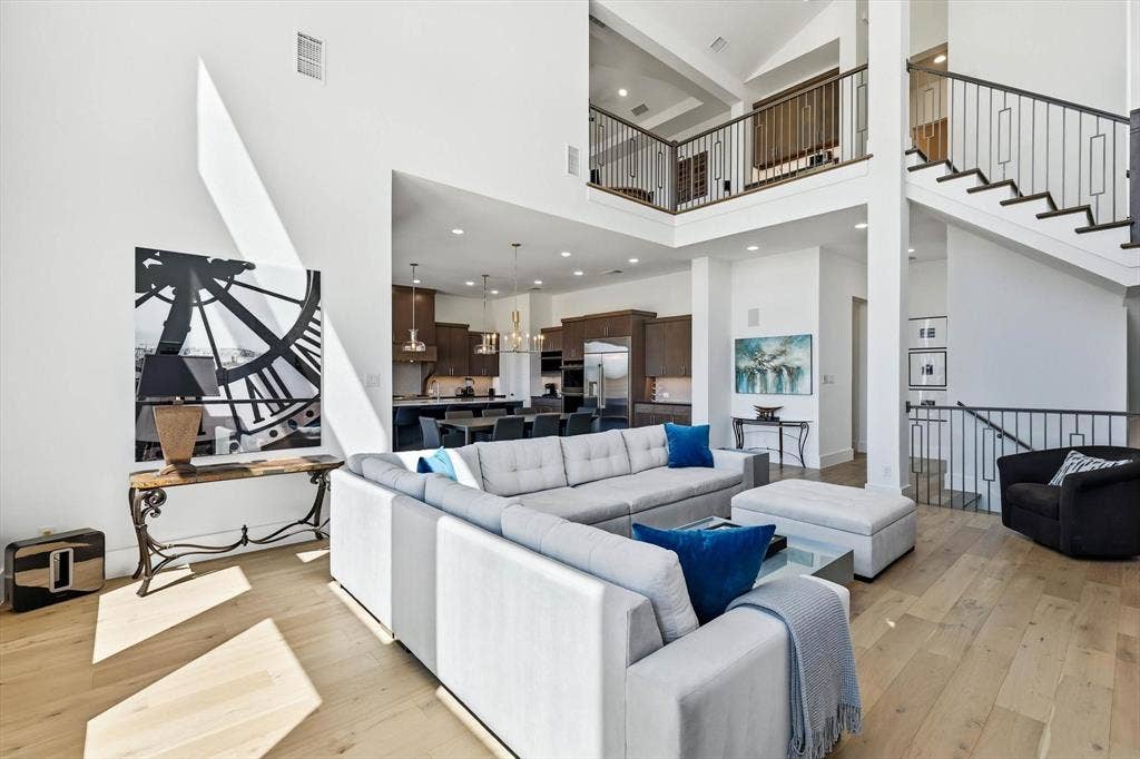 7853 Element Avenue, Plano, TX 75024 Open-concept floor plan with soaring double-height ceilings, wood-finish flooring, and a staircase featuring wrought iron balusters