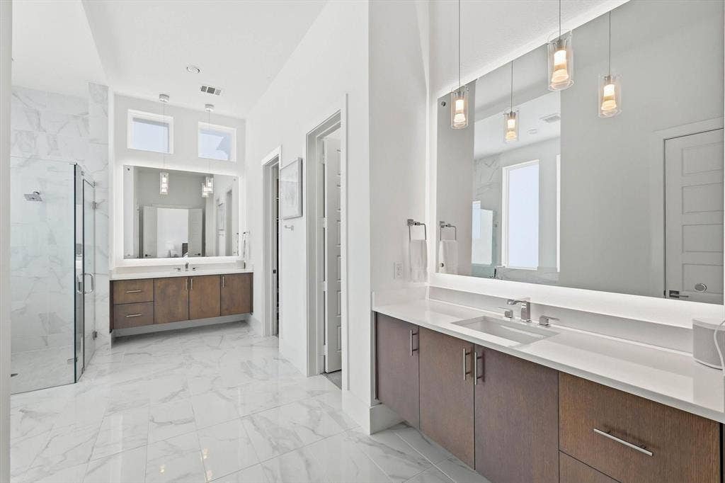 7853 Element Avenue, Plano, TX 75024 Bathroom featuring dual wood-finish vanities with quartz countertops, large backlit mirrors, pendant lighting, and oversized light-toned tile flooring