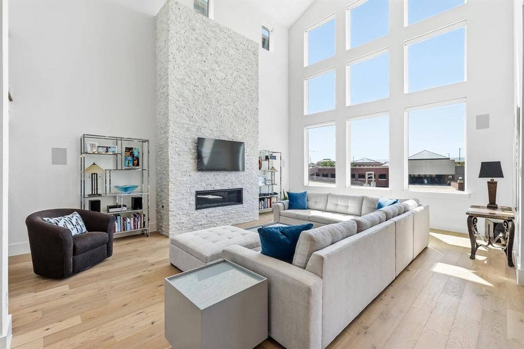 7853 Element Avenue, Plano, TX 75024 Double-height ceiling, floor-to-ceiling multi-pane windows, and a full-height stone-clad fireplace featuring a linear built-in hearth, complemented by light wood-finish flooring