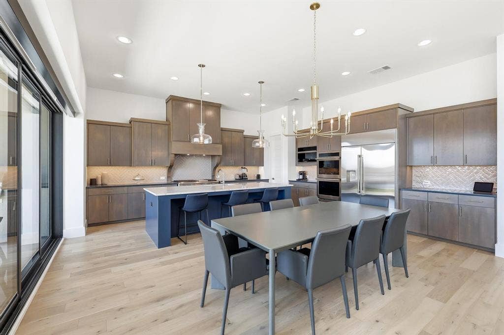 7853 Element Avenue, Plano, TX 75024 Kitchen featuring wood-finish flooring, two-tone cabinetry with a contrasting island, stone-surfaced countertops, herringbone-patterned tile backsplash, and built-in double wall ovens
