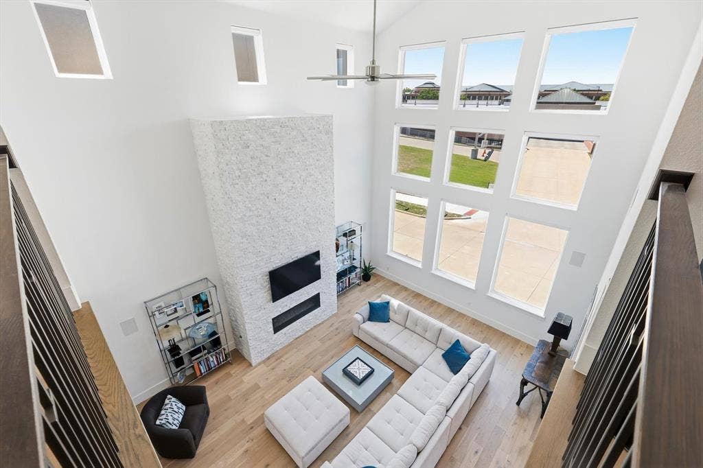 7853 Element Avenue, Plano, TX 75024 Vaulted ceilings featuring expansive floor-to-ceiling windows, white stone-textured fireplace surround, built-in linear fireplace, and wood-finish flooring