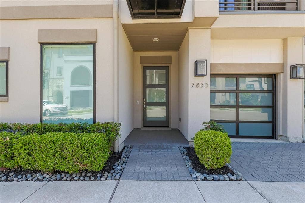 7853 Element Avenue, Plano, TX 75024 Contemporary exterior entrance featuring a modern glass-panel entry door, multi-pane frosted glass garage door, structured hedges, and a paver stone walkway