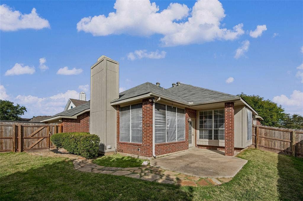 714 Cottonwood Bend Drive, Allen, TX 75002 Rear exterior featuring brick siding, a concrete patio, a tall brick chimney, and a wooden privacy fence enclosing the grass yard
